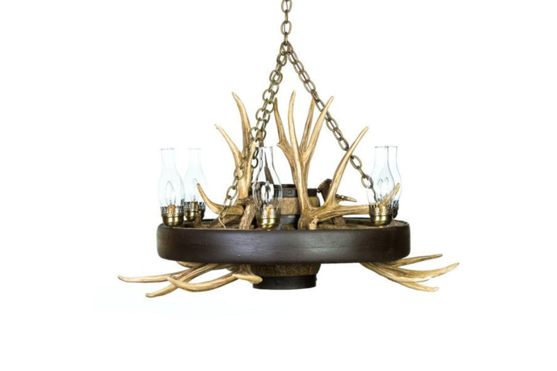 A rustic wagon wheel chandelier with mule deer antlers and chimney glass covering the lights.