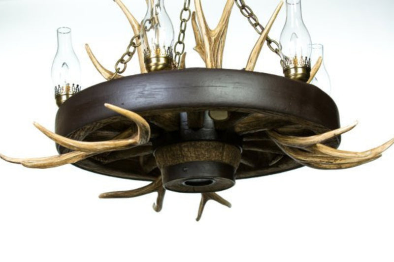 A rustic wagon wheel chandelier with mule deer antlers and chimney glass covering the lights.