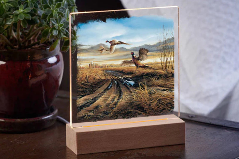 Acrylic night light featuring the artwork by Terry Redlin. The acrylic panel fits into a wood base and is powered by a 57 inch USB cable. The image shows three pheasants in flight over a country road. 