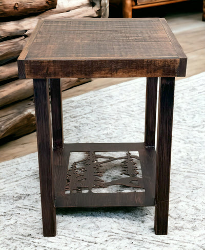 Pine  tree design metal leg end table with rough sawn wood top, displayed on wood floor with rustic logs in the background. 